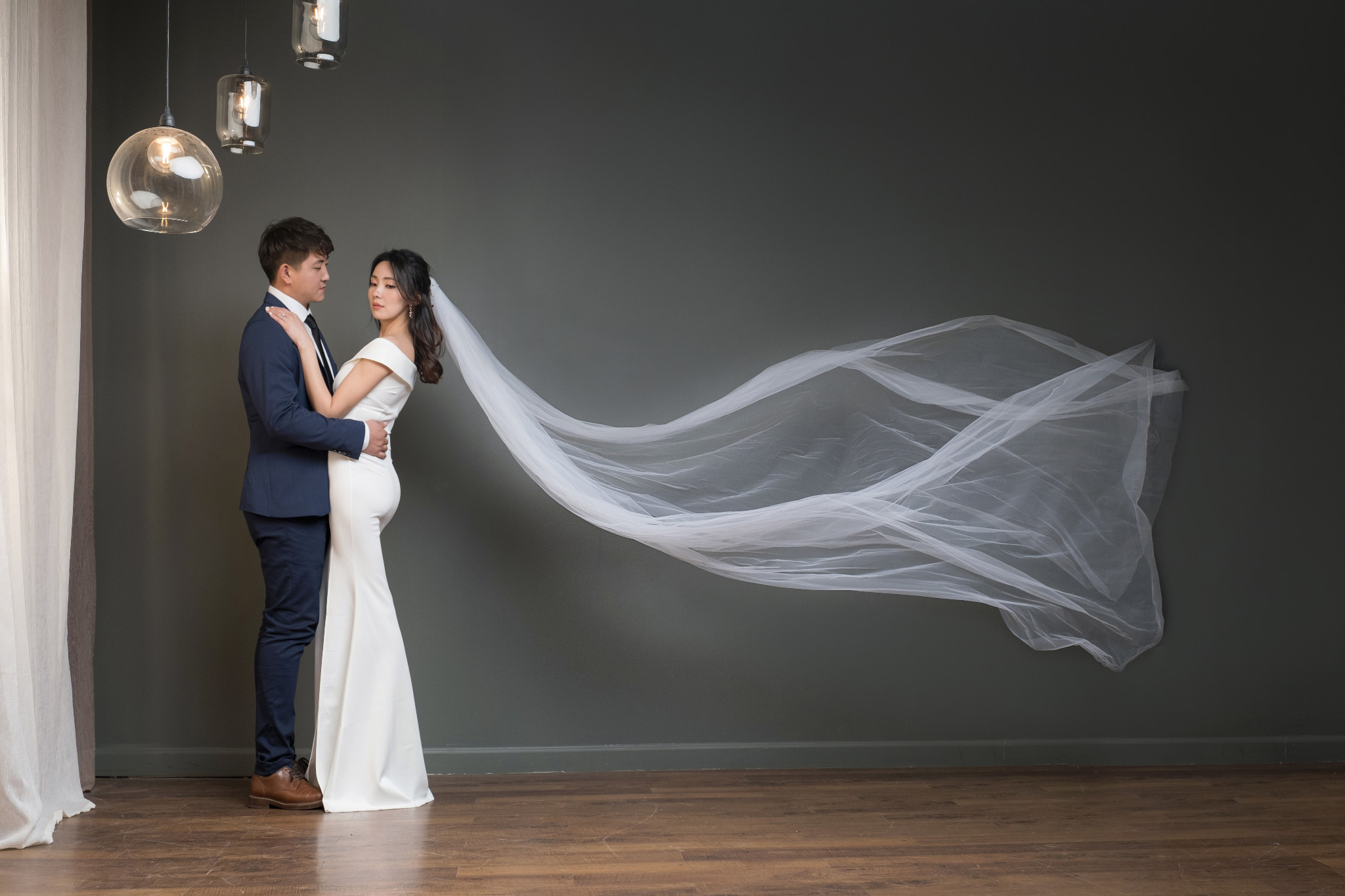 Couple in wedding clothing with a long white veil flowing across the studio