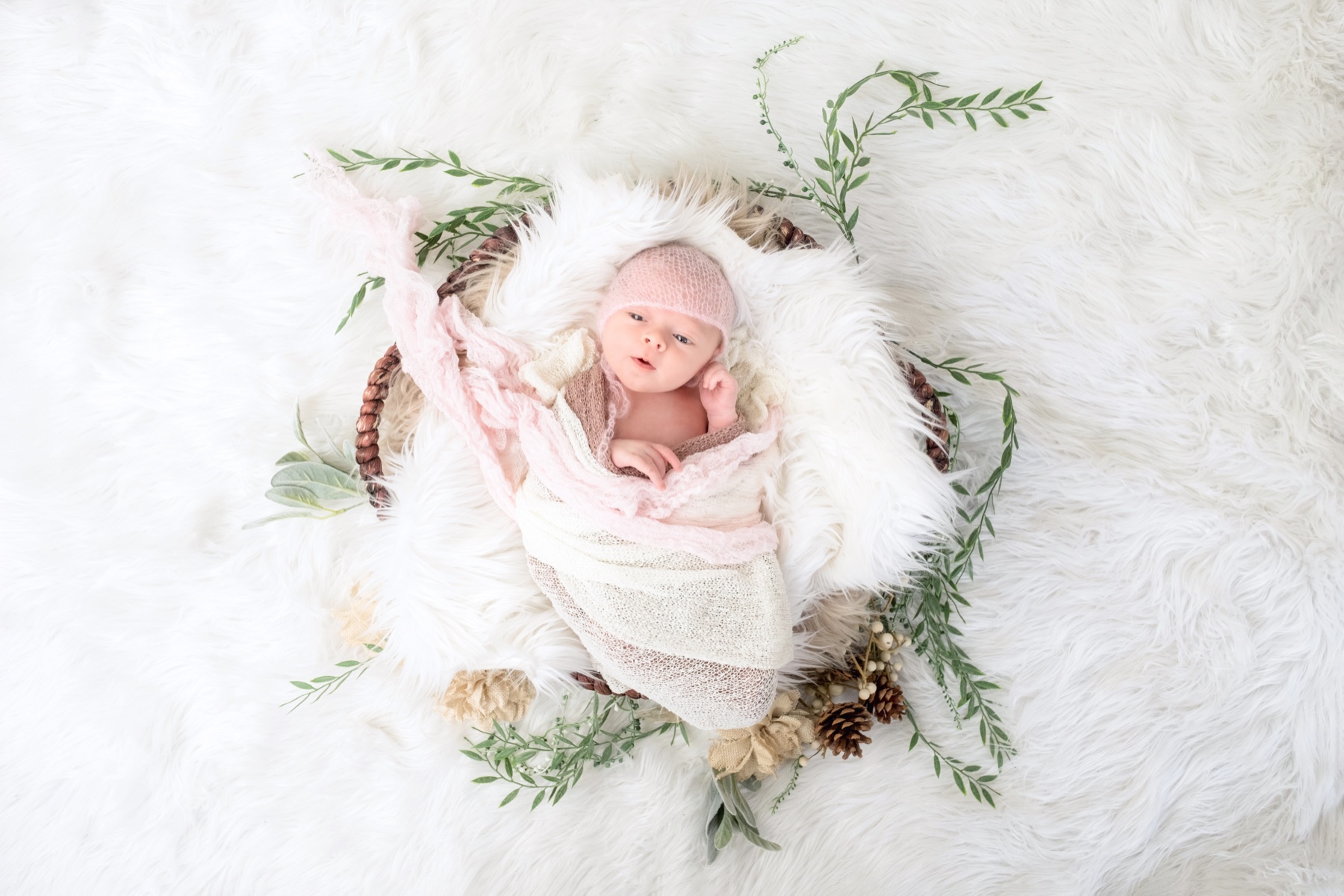 Newborn resting in a soft wrap among pale greenery