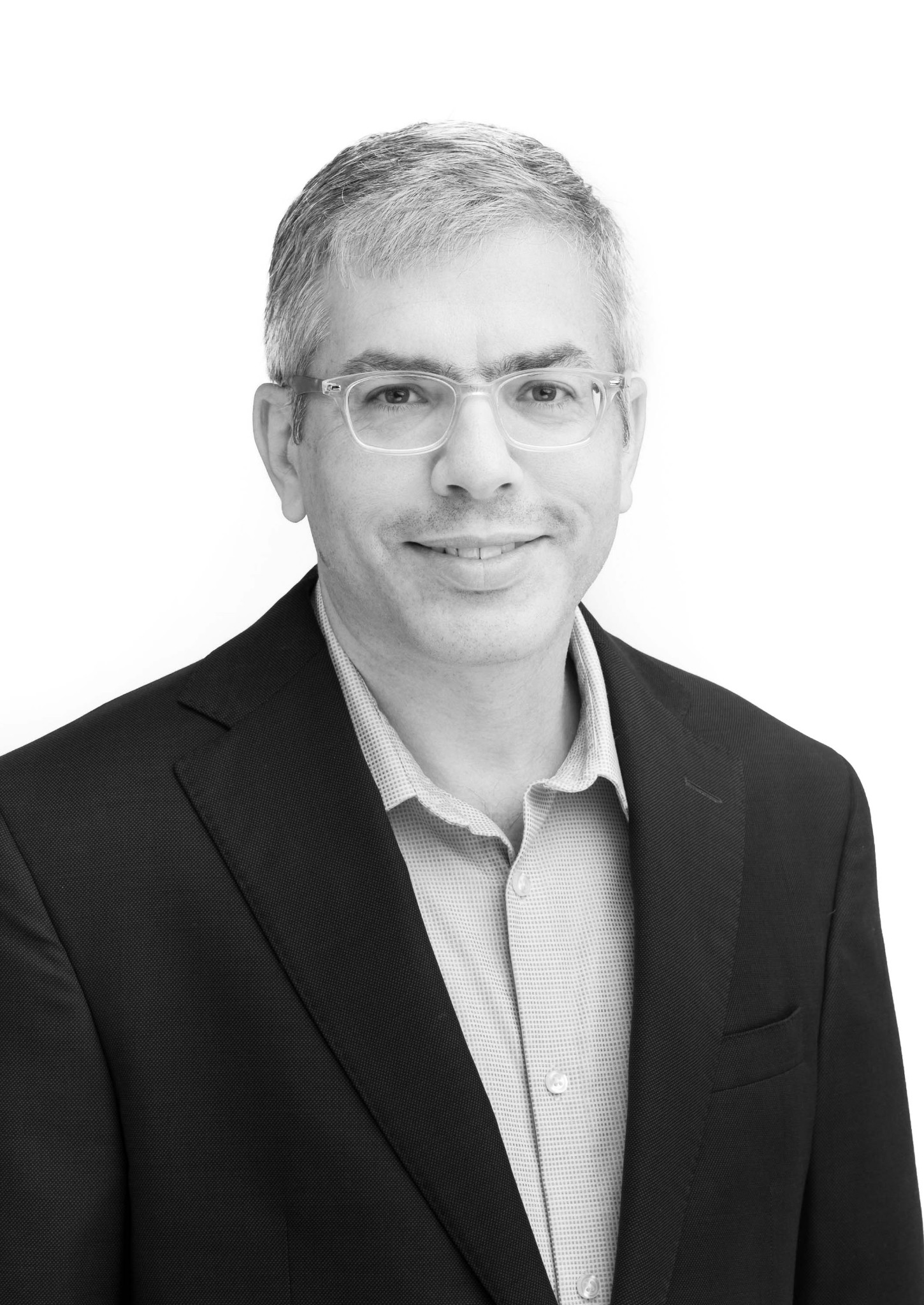 Black-and-white portrait of a person wearing glasses and a jacket against a light background.