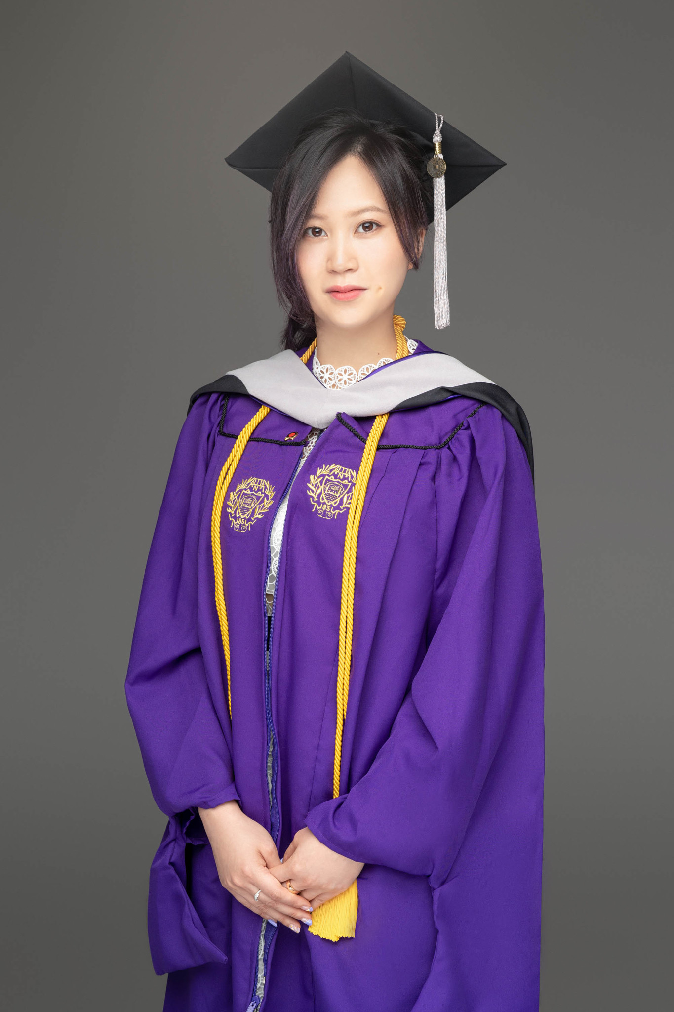 Person wearing a black graduation cap and a purple academic gown with gold cords.