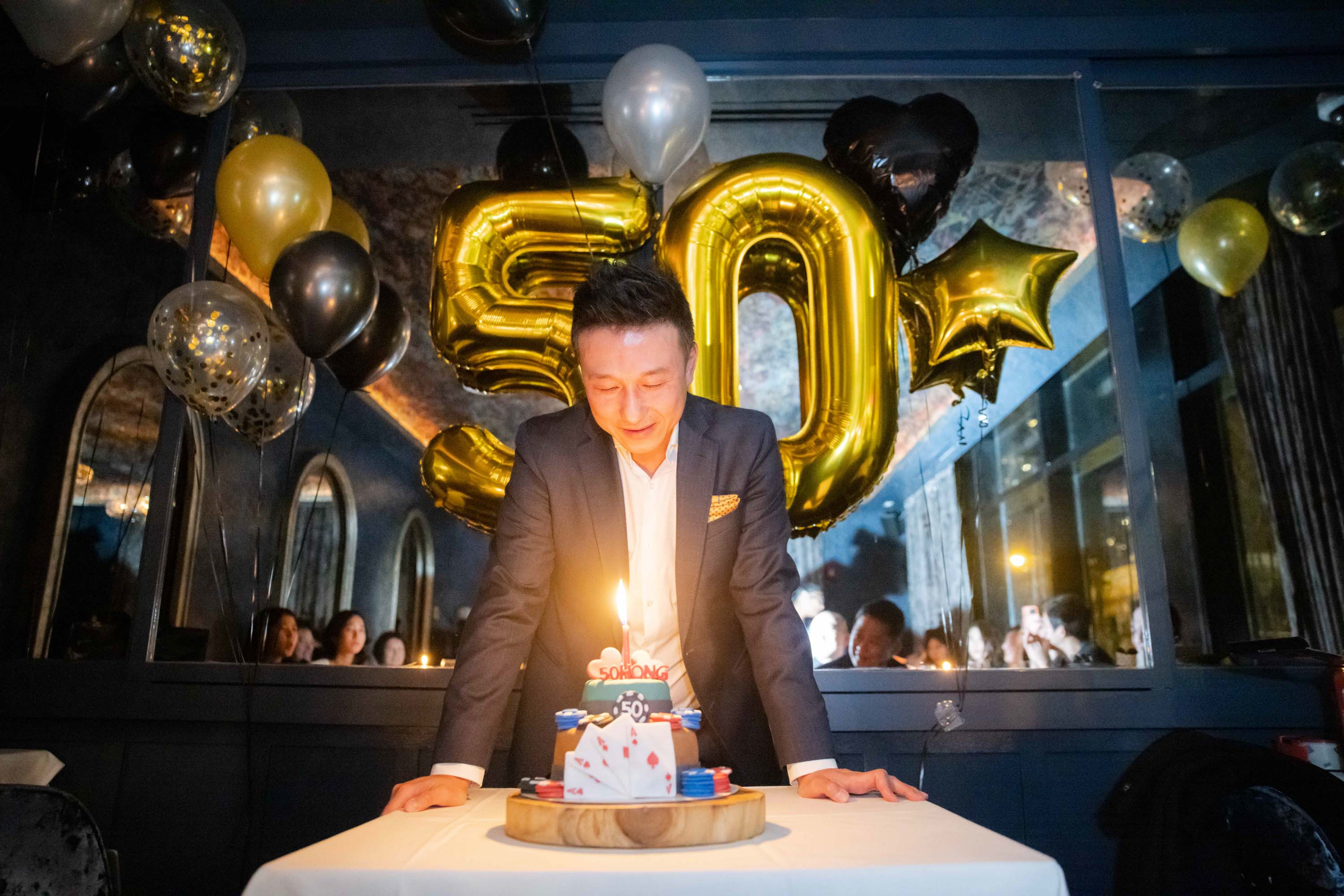 A birthday gathering with a cake, guests and gold balloons