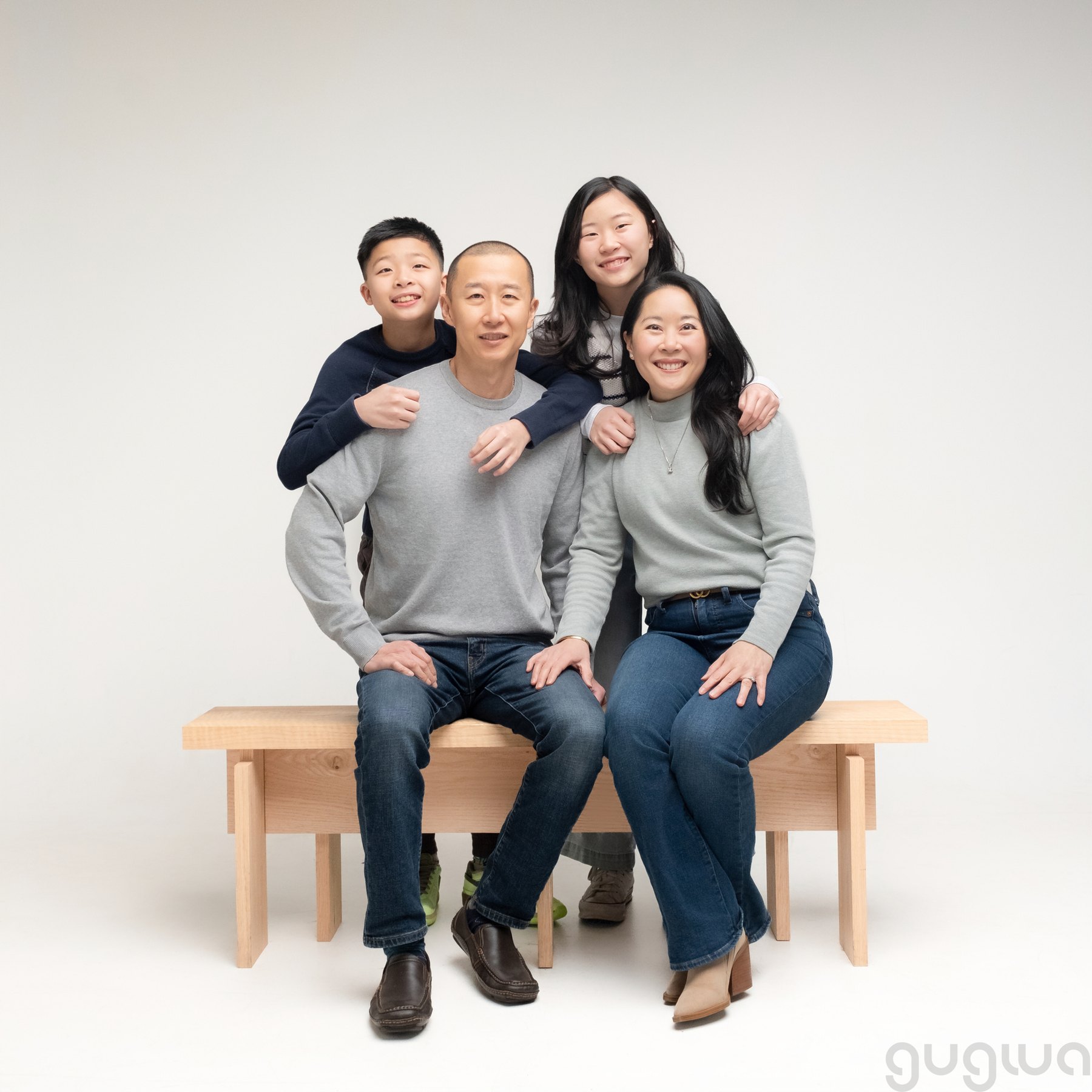 Four people posing together, with two seated on a wooden bench and two standing behind them.