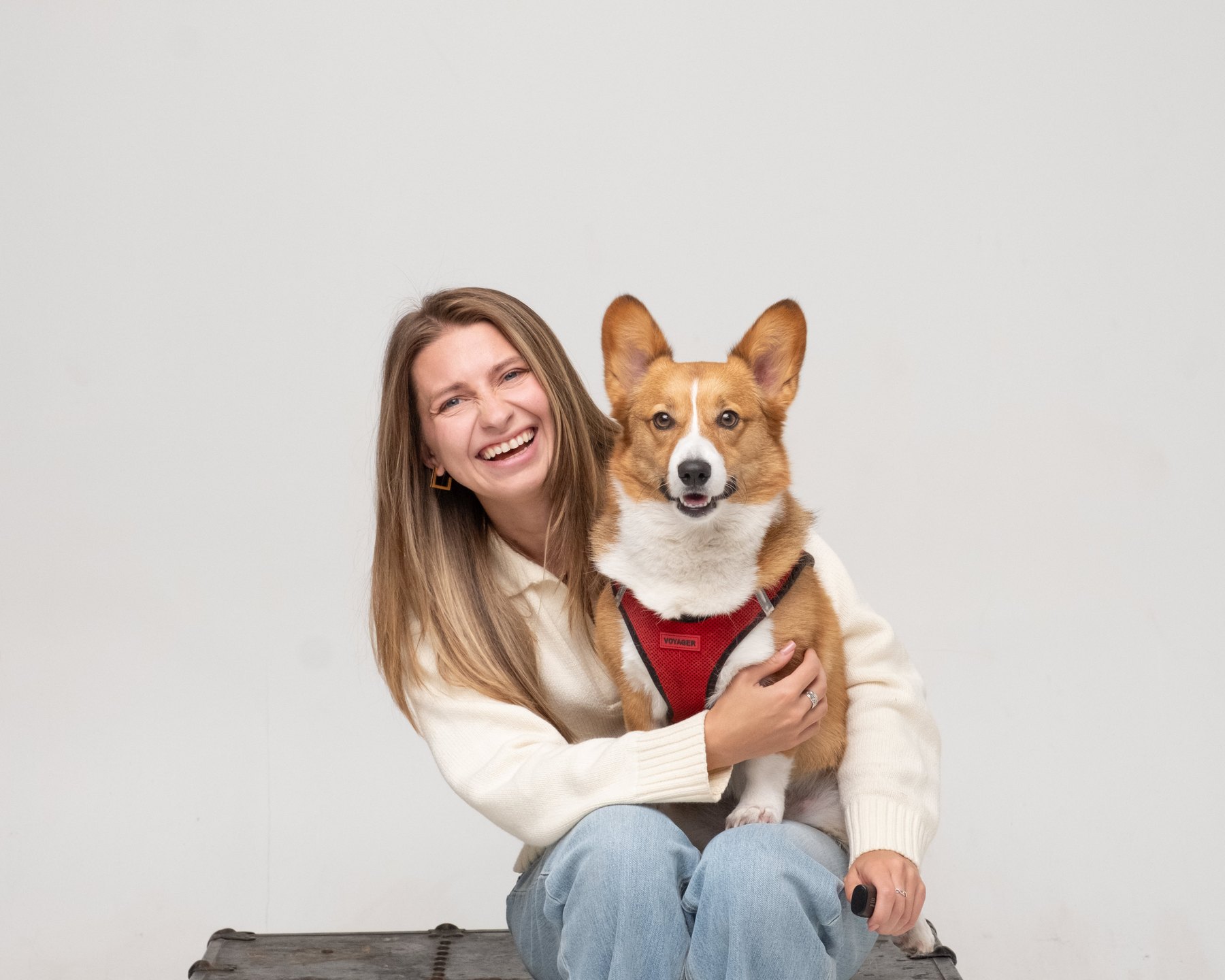 Smiling person in a cream sweater, seated holding a brown-and-white dog.