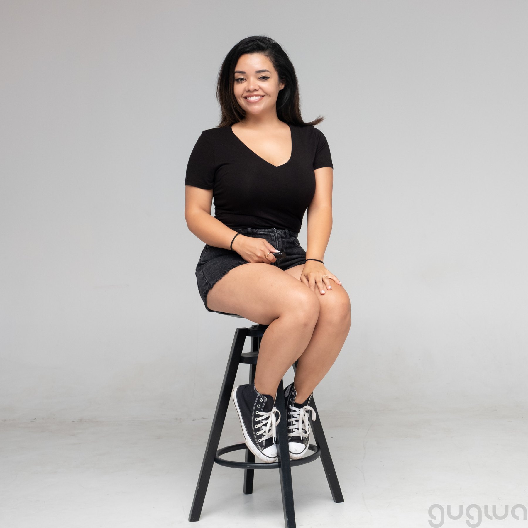 Smiling person in a black T-shirt seated on a tall black stool.